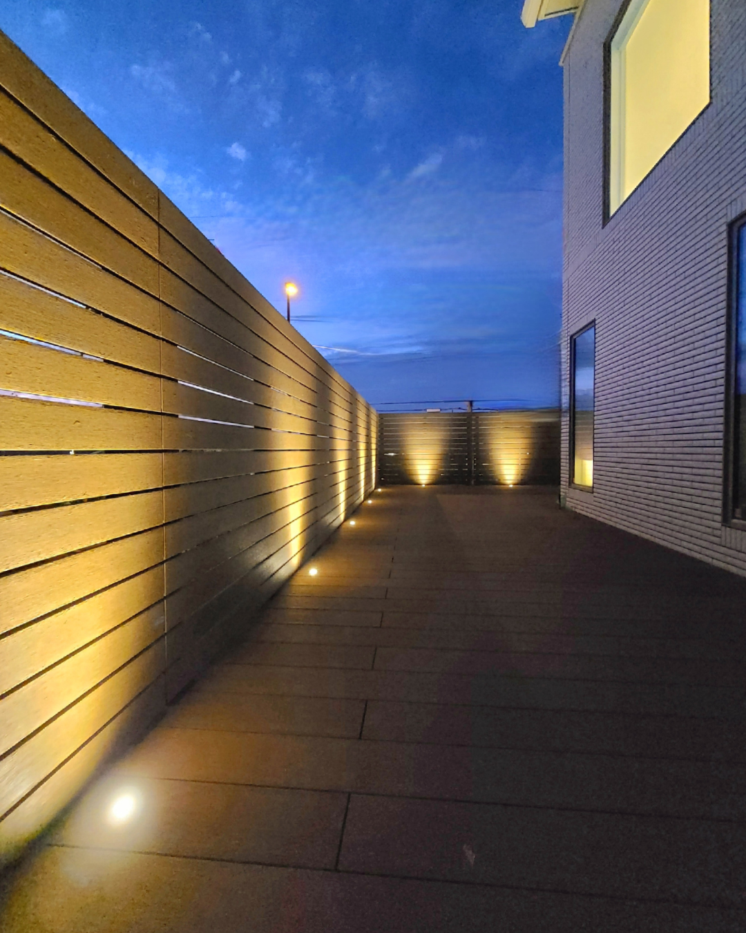 ライトアップが美しいウッド調フェンスの夜のアプローチ外構